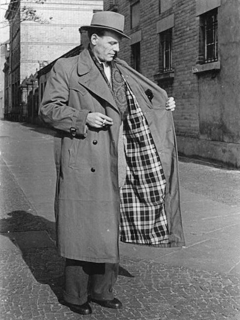 Man i klassisk trenchcoat visar upp det rutiga fodret på en gata